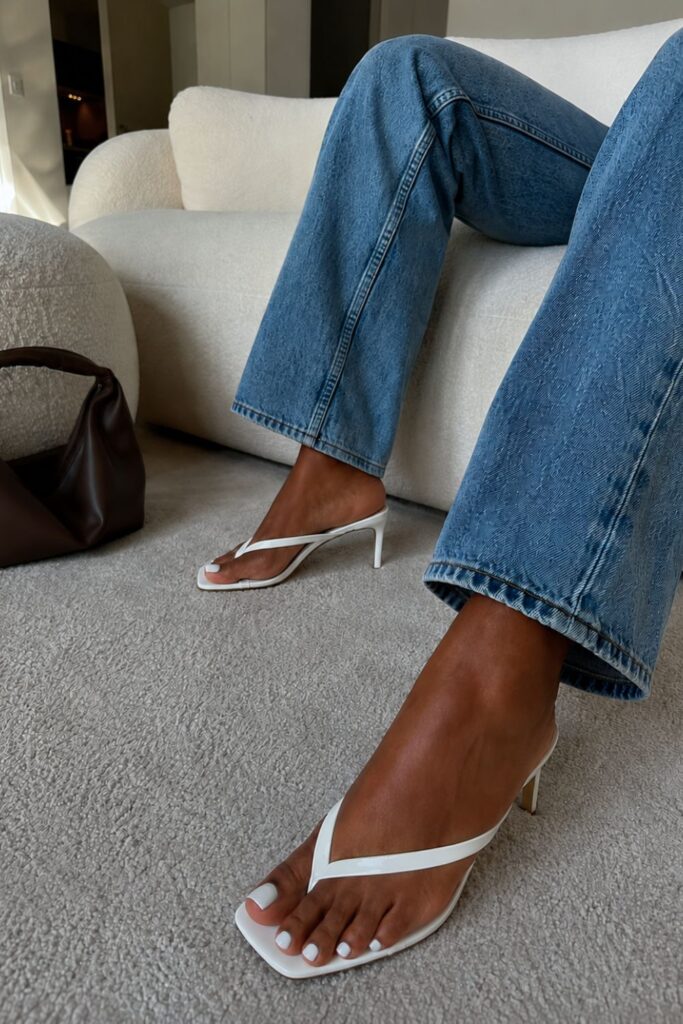 White toe-post heels styled with straight-leg blue jeans in a minimal, neutral outfit