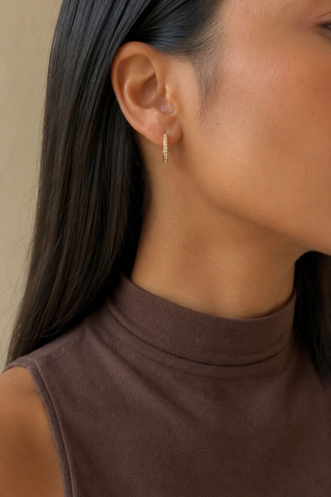 Close-up of a woman wearing yellow gold pavé diamond hoop earrings with sleek dark hair and a sleeveless brown mock-neck top