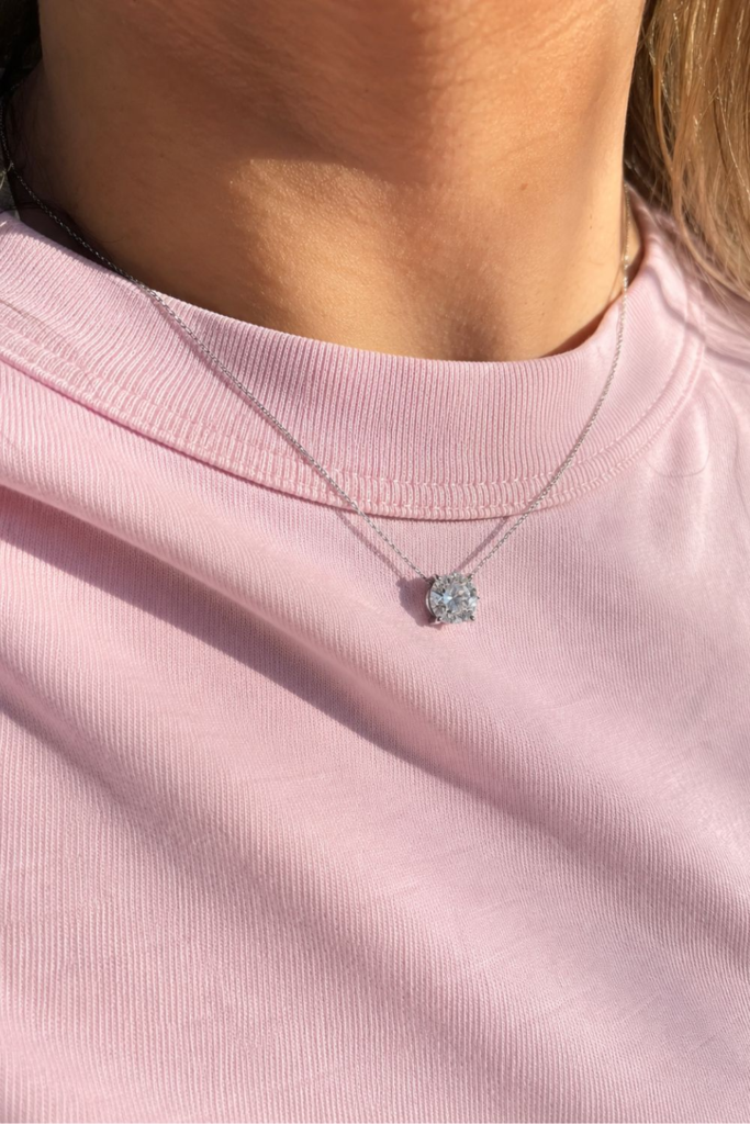 Woman wearing a solitaire diamond pendant necklace with a light pink crew neck top, showcasing minimalist accessories
