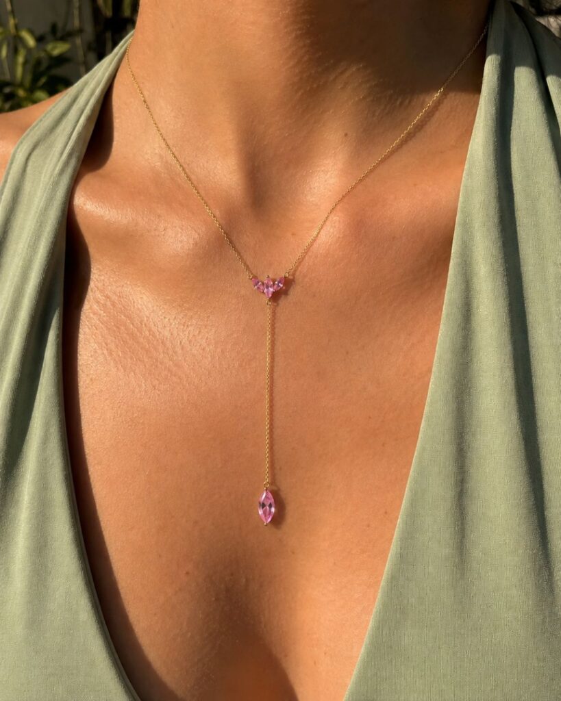 Delicate gold Y-necklace with pink sapphire pendants styled with a sage green halter top, showcasing elegant accessories that elevate an outfit