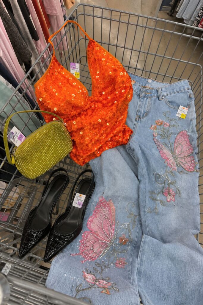 Thrift store shopping cart with curated secondhand fashion finds—sequin top, embroidered jeans, rhinestone bag, and black heels—illustrating how to explore and find your personal style through vintage shopping