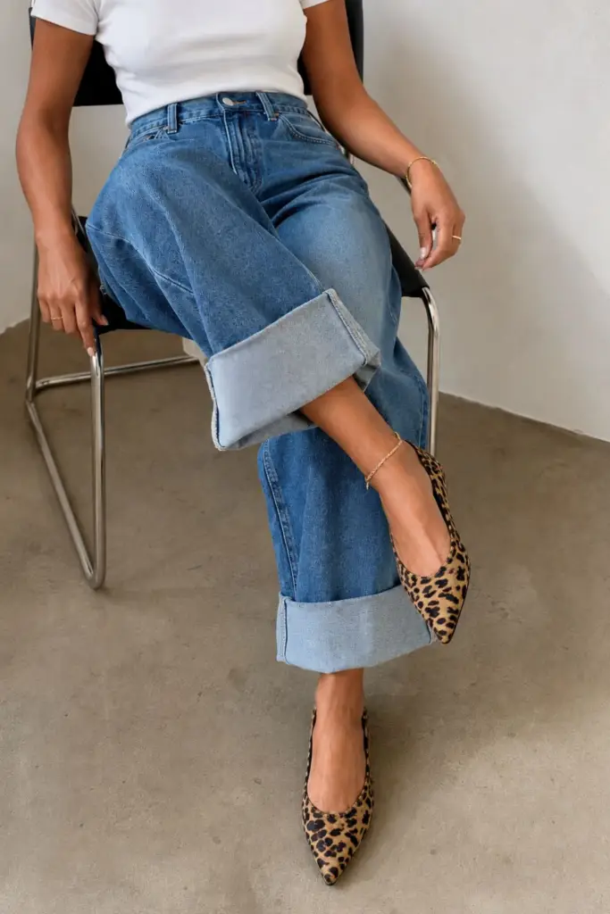 Woman wearing a fitted white T-shirt with cuffed wide-leg jeans and leopard print pointed-toe flats in a minimalist outfit